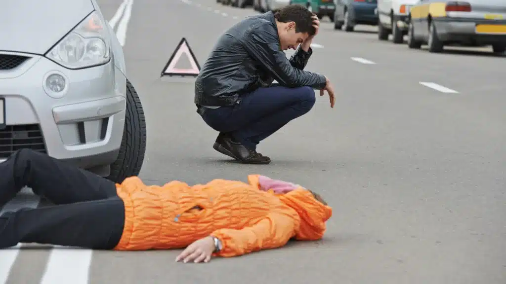 Injured pedestrian lying on the street after a car accident with bystander nearby.