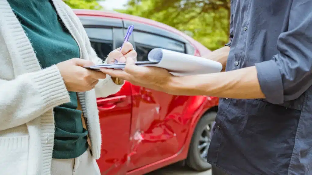 Insurance adjuster documenting damage to a red car after an accident