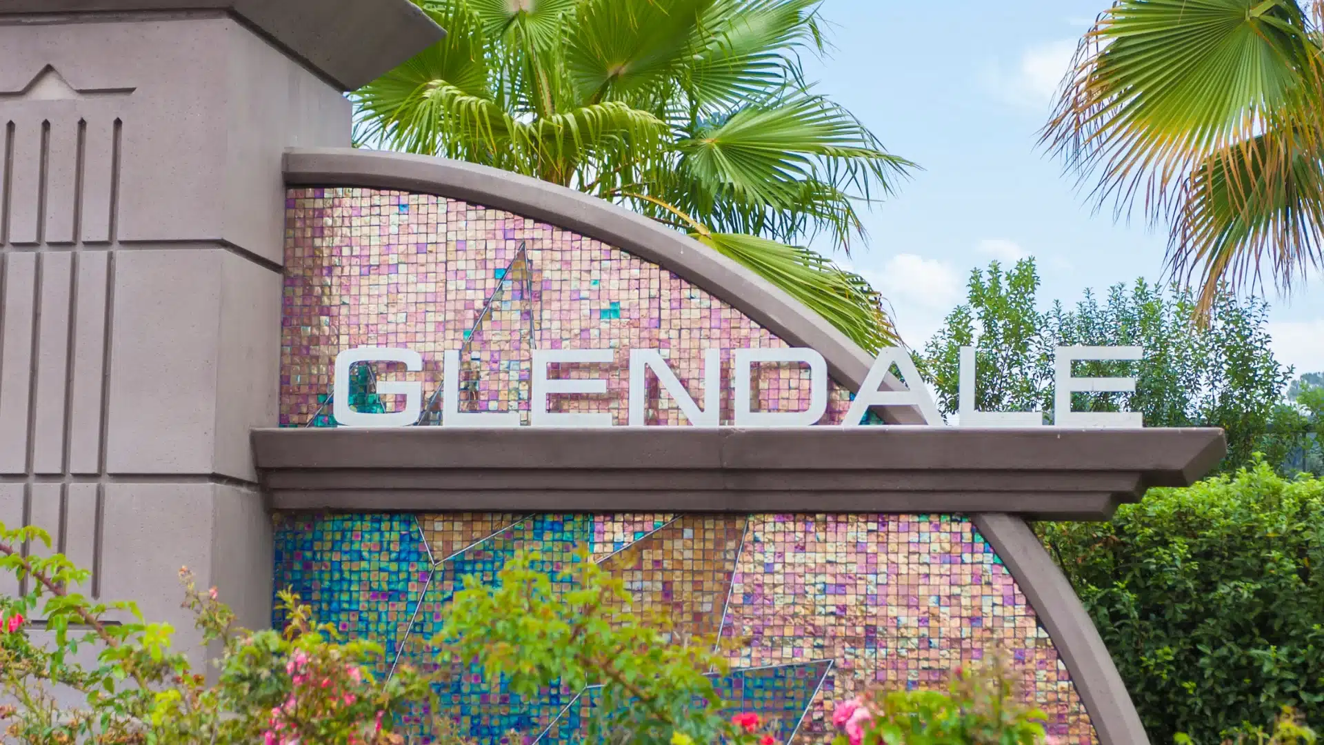Glendale, California city sign with mosaic design surrounded by greenery and palm trees.