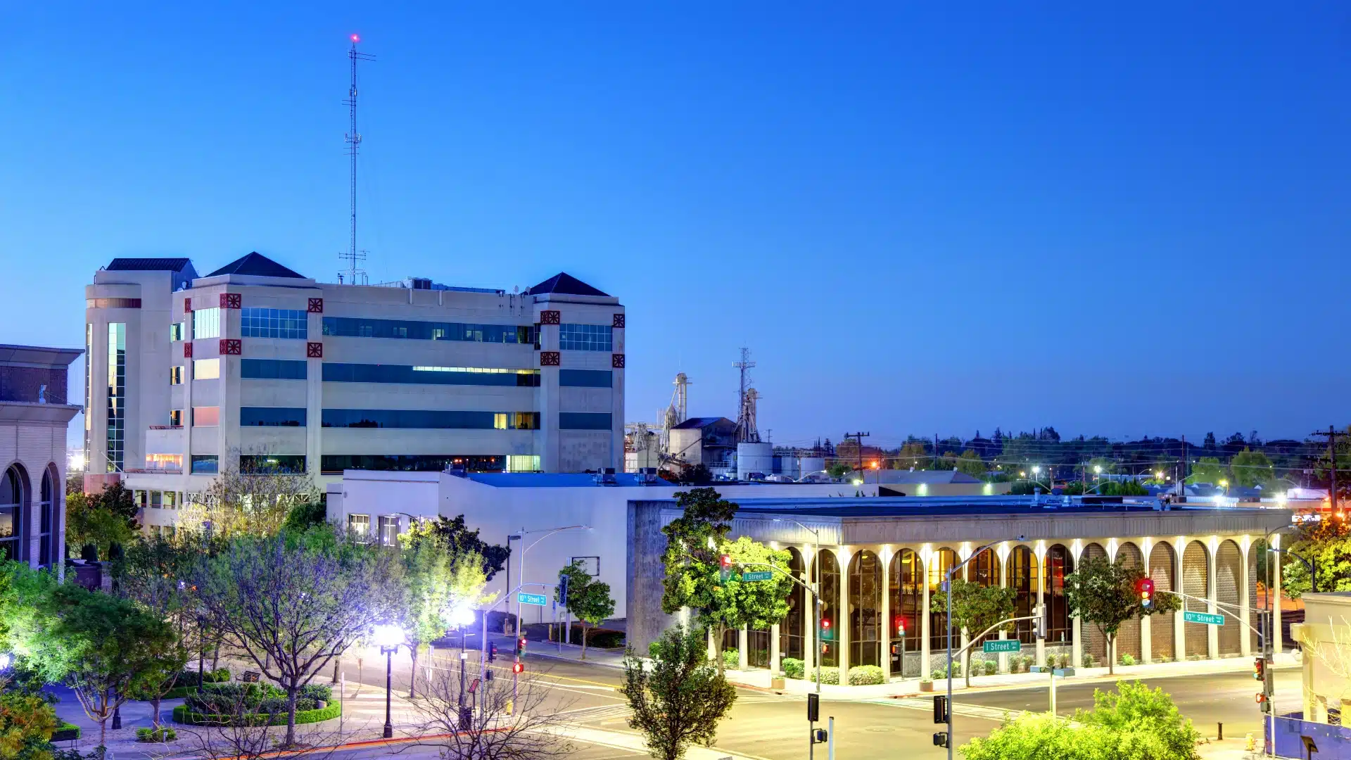 Downtown Modesto, California at dusk with modern buildings and illuminated street scene.