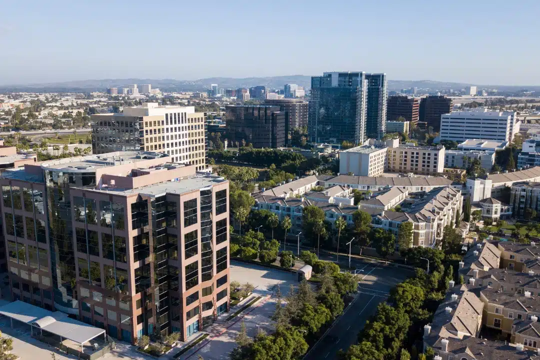 Aerial view of a modern urban district with office buildings, apartment complexes, tree-lined streets, and a clear sky.