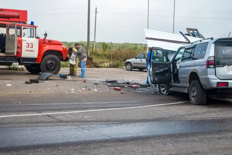 Damaged SUV and fire truck at a highway crash scene with debris scattered across the road.